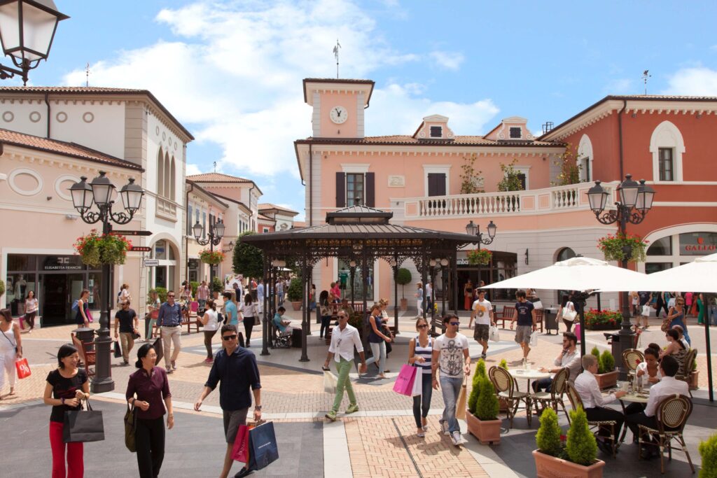 GCC Tourists Relaxing In A Stylish Courtyard At Noventa Di Piave, A McArthurGlen Designer Outlet Near Venice.